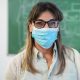 Happy latin teacher smiling on camera while wearing safety masks inside class room - Focus on nose